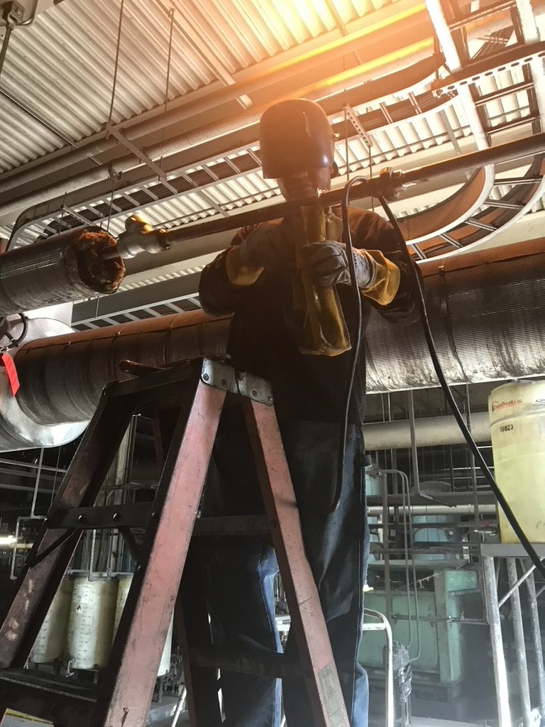 Welder making an overhead code weld on plant piping