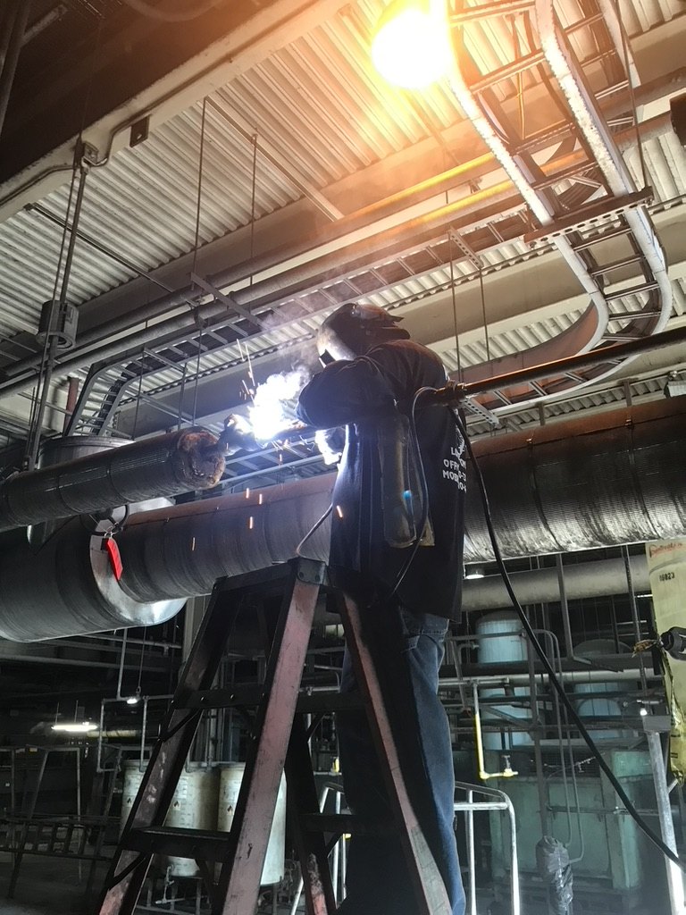 Welder arc-welding overhead pipe inside an industrial plant